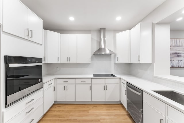 kitchen with wall chimney range hood, sink, light hardwood / wood-style flooring, stainless steel appliances, and white cabinets