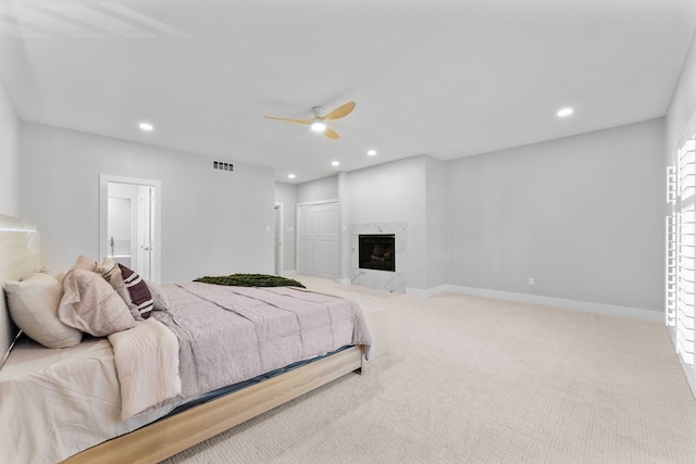 bedroom featuring ceiling fan, connected bathroom, a premium fireplace, and light colored carpet