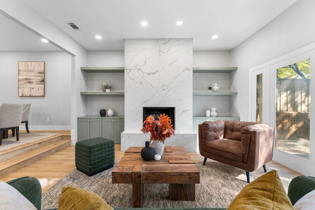 living room with built in shelves, a high end fireplace, and light hardwood / wood-style flooring