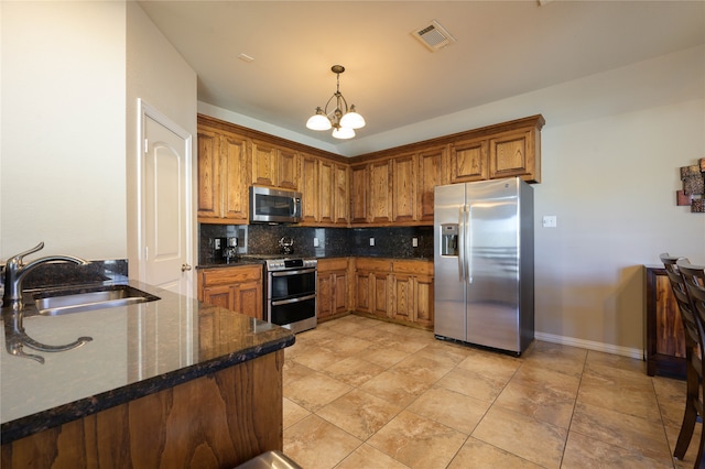 kitchen with dark stone countertops, sink, pendant lighting, appliances with stainless steel finishes, and tasteful backsplash