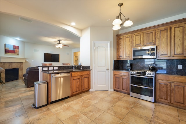 kitchen with tasteful backsplash, appliances with stainless steel finishes, dark stone countertops, ceiling fan with notable chandelier, and decorative light fixtures