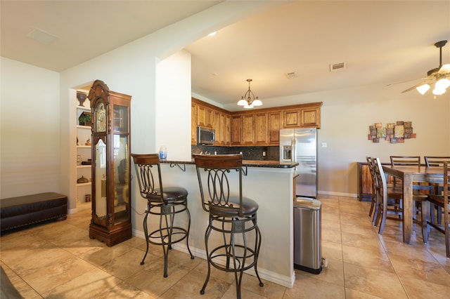 kitchen featuring a kitchen bar, ceiling fan with notable chandelier, backsplash, kitchen peninsula, and stainless steel appliances