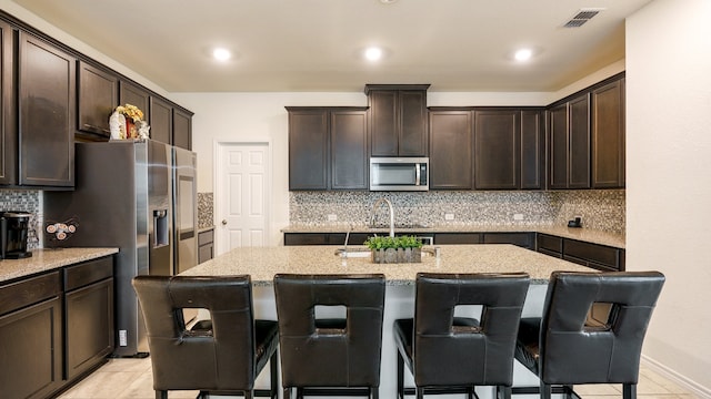 kitchen featuring stainless steel appliances, tasteful backsplash, a breakfast bar area, and an island with sink