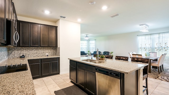 kitchen with sink, an island with sink, a kitchen breakfast bar, stainless steel appliances, and light stone counters