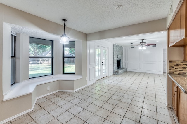 interior space with ceiling fan, a fireplace, a textured ceiling, and light tile patterned floors