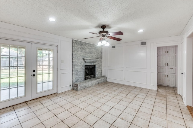 unfurnished living room with light tile patterned floors, ceiling fan, a fireplace, a textured ceiling, and french doors