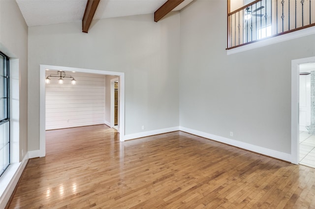 unfurnished living room featuring a towering ceiling, light hardwood / wood-style flooring, and beamed ceiling