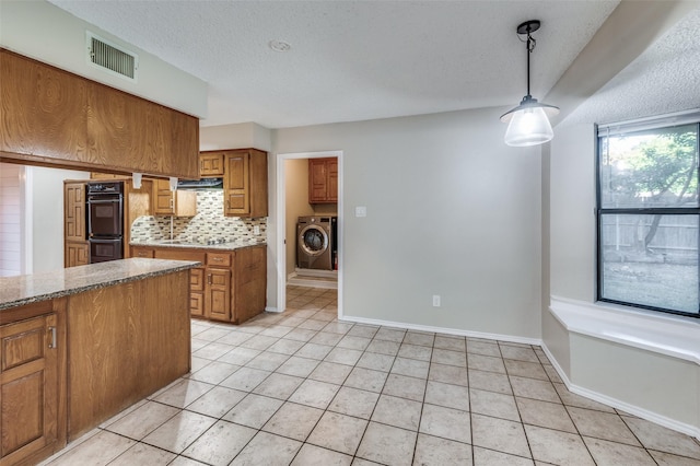 kitchen with pendant lighting, tasteful backsplash, washer / dryer, light tile patterned floors, and black appliances