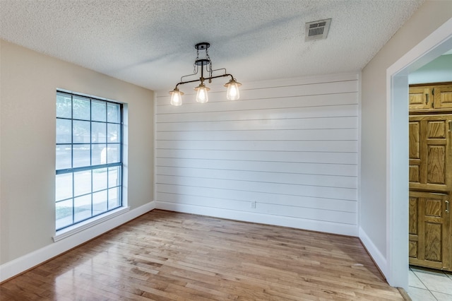 unfurnished dining area with an inviting chandelier, wooden walls, light hardwood / wood-style flooring, and a textured ceiling