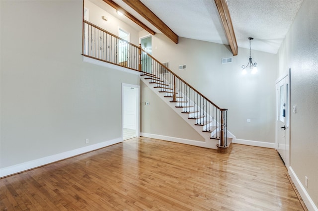 interior space with a chandelier, high vaulted ceiling, a textured ceiling, beam ceiling, and light hardwood / wood-style floors