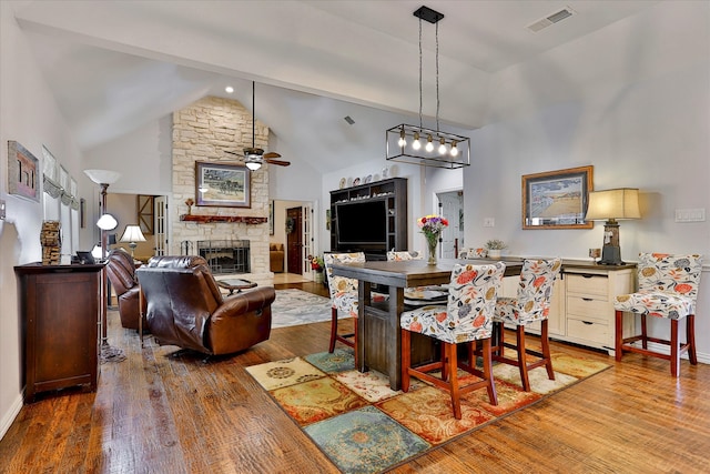 dining area with a stone fireplace, high vaulted ceiling, wood-type flooring, and ceiling fan