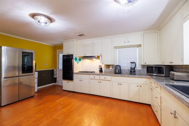 kitchen with crown molding, white cabinets, stainless steel appliances, and light hardwood / wood-style floors