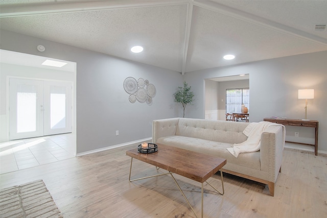 living room with french doors, lofted ceiling with beams, a textured ceiling, and light wood-type flooring