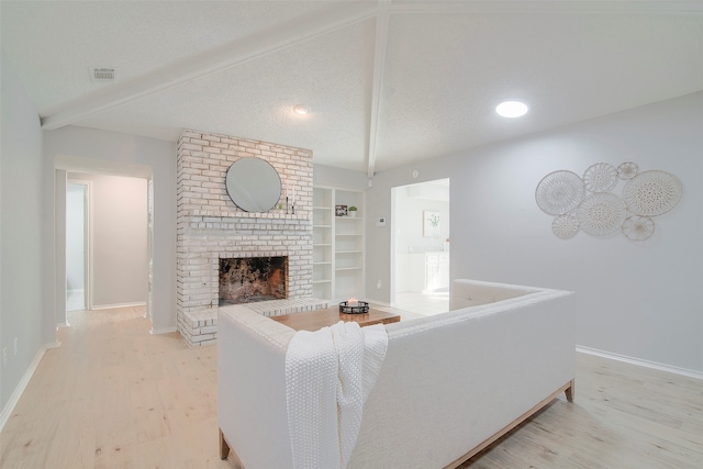 living room with a textured ceiling, light wood-type flooring, vaulted ceiling, built in features, and a fireplace