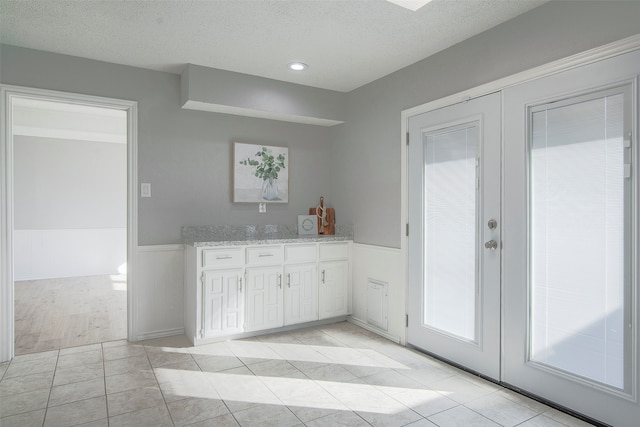 kitchen featuring light stone countertops, french doors, a textured ceiling, white cabinets, and light tile patterned floors