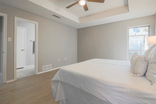 bedroom with hardwood / wood-style floors, a tray ceiling, a textured ceiling, and ceiling fan