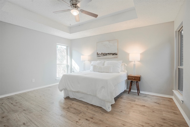 bedroom featuring a textured ceiling, a tray ceiling, light wood-type flooring, and ceiling fan