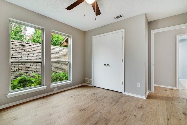 unfurnished bedroom with light hardwood / wood-style floors, a closet, a textured ceiling, and ceiling fan