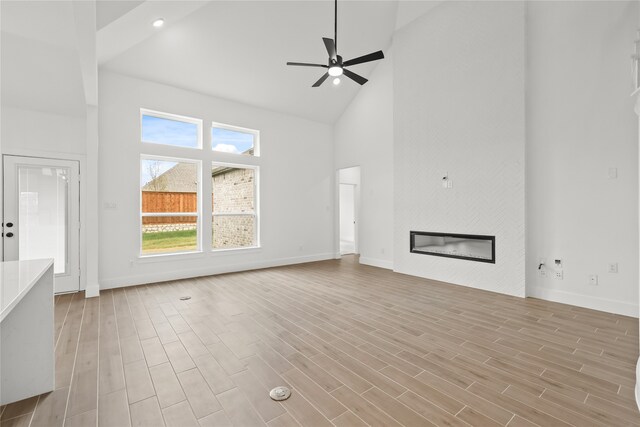 unfurnished living room with light hardwood / wood-style floors, high vaulted ceiling, and ceiling fan