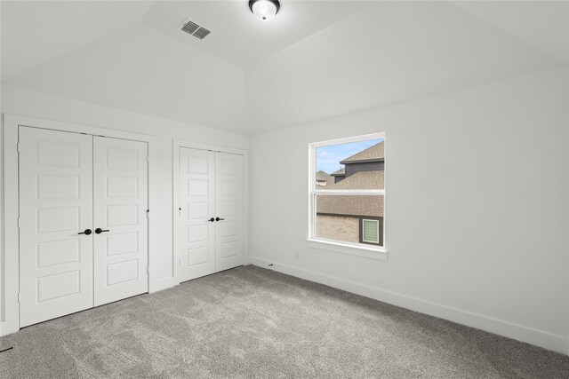 unfurnished bedroom with carpet, vaulted ceiling, and two closets