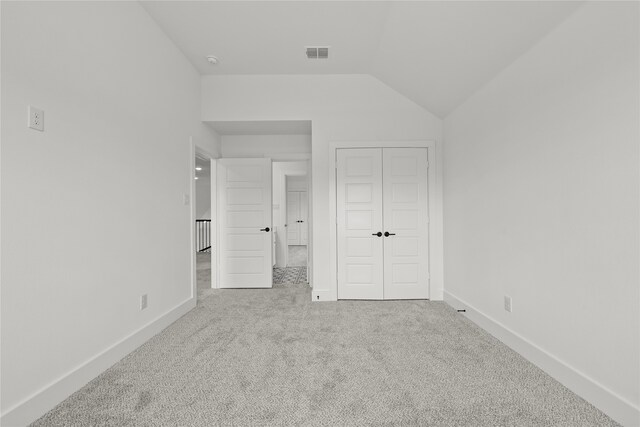 unfurnished bedroom with a closet, light carpet, and lofted ceiling