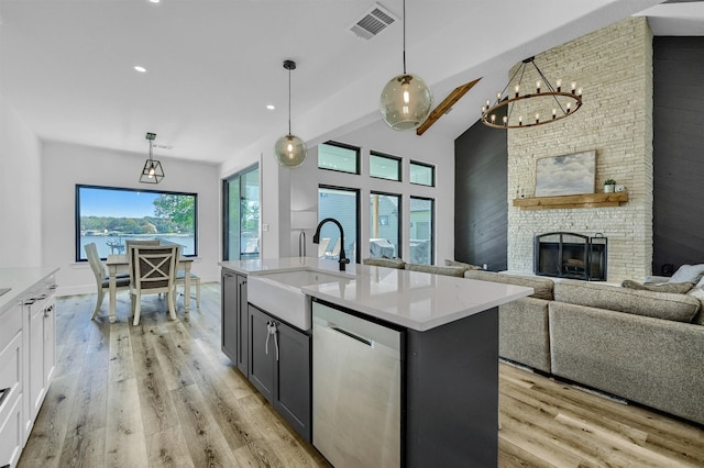 kitchen featuring a stone fireplace, stainless steel dishwasher, a center island with sink, and hanging light fixtures