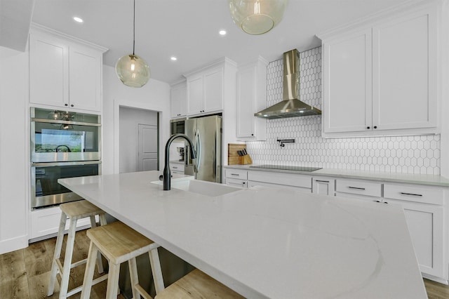 kitchen with light hardwood / wood-style floors, wall chimney exhaust hood, white cabinets, and stainless steel appliances