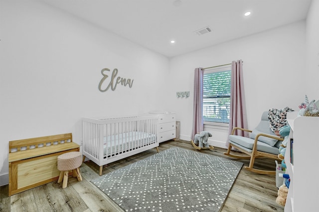 bedroom with a crib and wood-type flooring