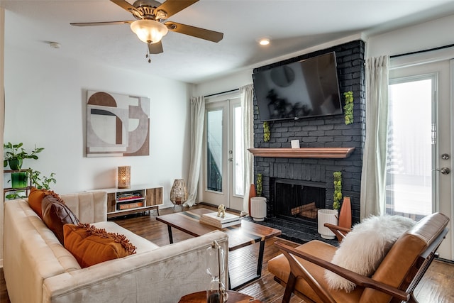 living room with hardwood / wood-style floors, a healthy amount of sunlight, ceiling fan, and a brick fireplace