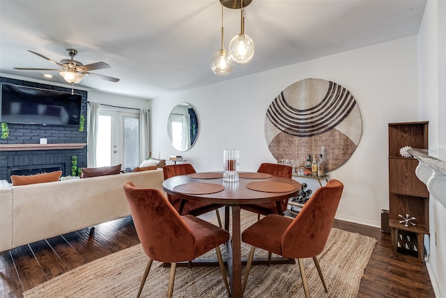 dining room featuring dark wood-type flooring, a brick fireplace, french doors, and ceiling fan