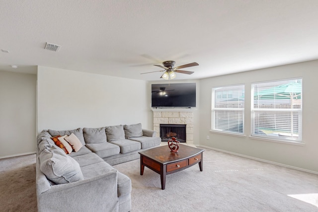 carpeted living room with a stone fireplace and ceiling fan