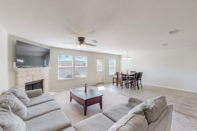 living room with a fireplace, a textured ceiling, light wood-type flooring, and ceiling fan