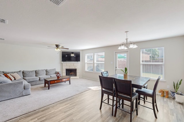 dining area with a stone fireplace, light hardwood / wood-style flooring, and ceiling fan with notable chandelier