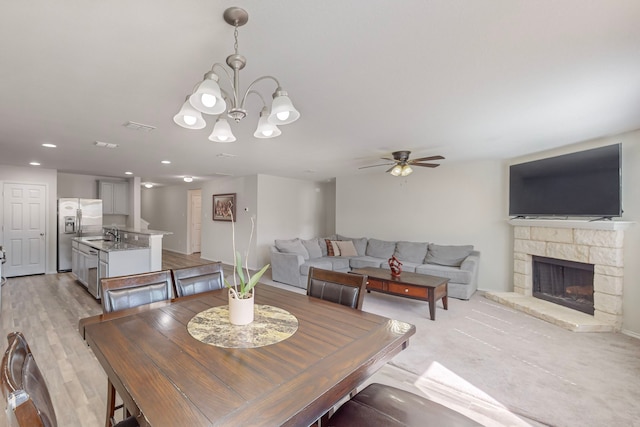 dining room with light hardwood / wood-style flooring, sink, ceiling fan with notable chandelier, and a fireplace