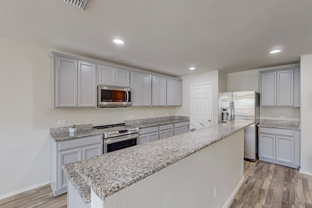 kitchen featuring a kitchen island, appliances with stainless steel finishes, light stone countertops, light hardwood / wood-style flooring, and gray cabinetry