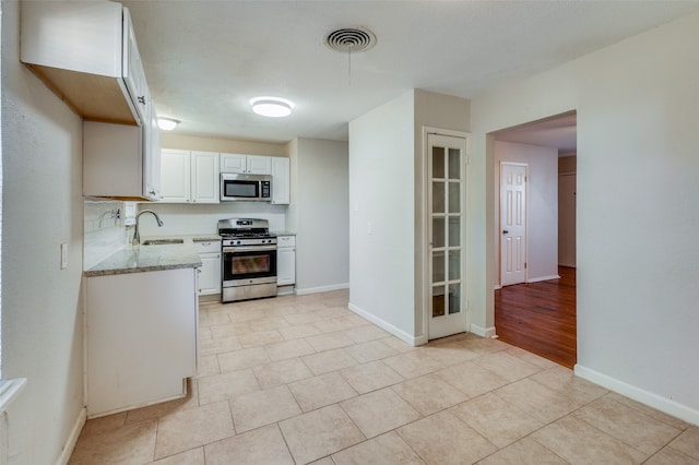 kitchen featuring white cabinets, appliances with stainless steel finishes, light stone countertops, light tile patterned flooring, and sink