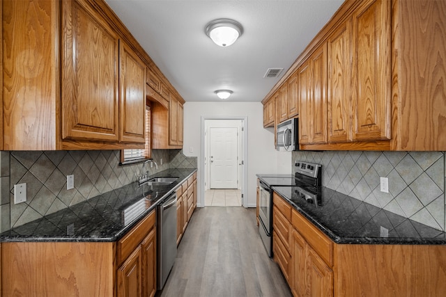 kitchen featuring hardwood / wood-style floors, stainless steel appliances, tasteful backsplash, and dark stone countertops