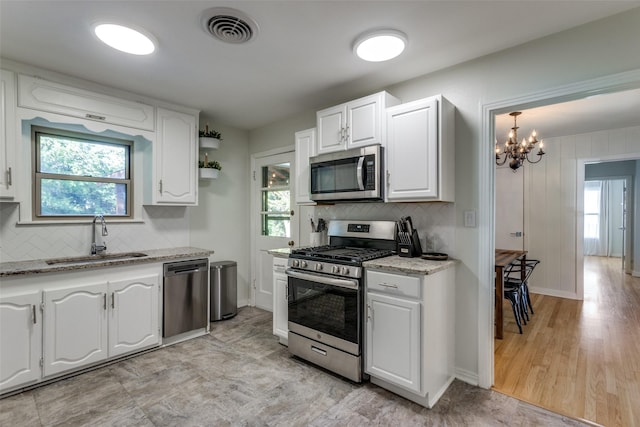 kitchen with appliances with stainless steel finishes, a sink, white cabinetry, and a chandelier