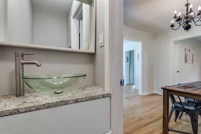 bathroom featuring wood finished floors, a chandelier, vanity, baseboards, and ornamental molding