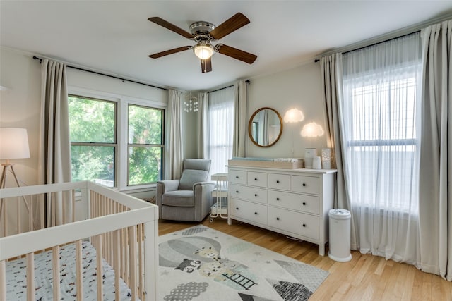 bedroom with a nursery area, light wood-style flooring, and ceiling fan