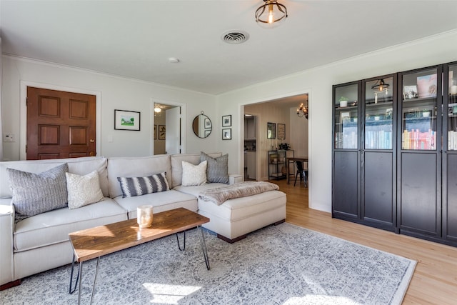 living area featuring light wood-type flooring, ornamental molding, and a chandelier