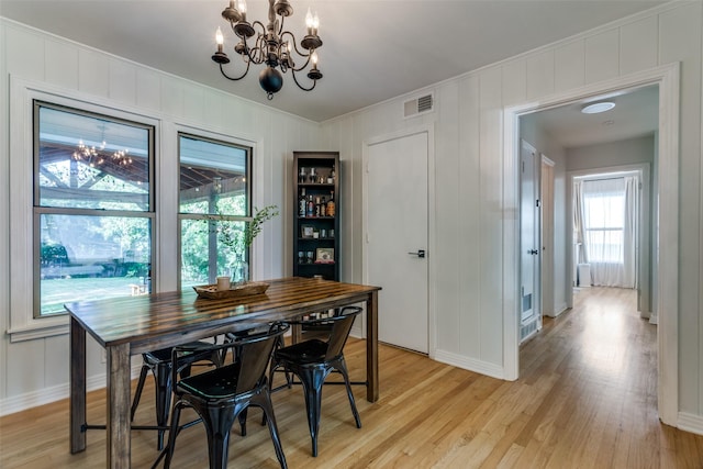 dining area with a chandelier, light wood-style floors, ornamental molding, a decorative wall, and baseboards