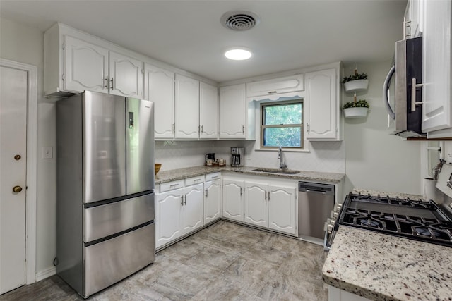 kitchen with stainless steel appliances, a sink, white cabinetry, and light stone countertops