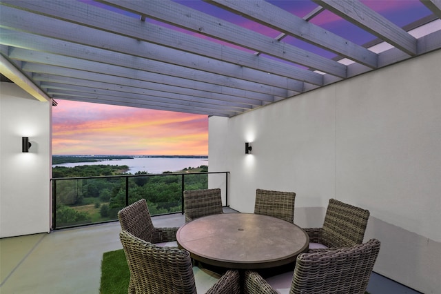 patio terrace at dusk featuring a pergola, a water view, and a balcony