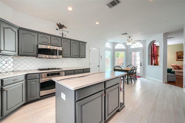 kitchen with appliances with stainless steel finishes, a center island, gray cabinets, and ceiling fan