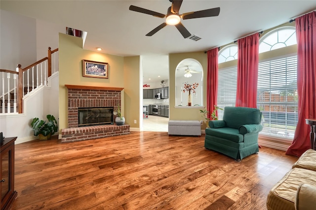 living room with ceiling fan, wood-type flooring, and a brick fireplace