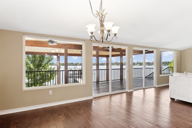 unfurnished dining area with ceiling fan with notable chandelier and dark hardwood / wood-style flooring