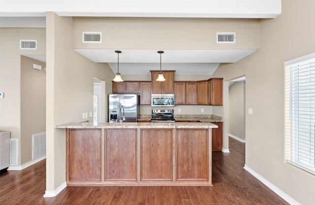 kitchen featuring dark wood-type flooring, appliances with stainless steel finishes, light stone counters, and pendant lighting