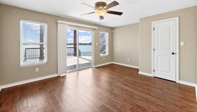 unfurnished room featuring dark wood-type flooring, a water view, and ceiling fan