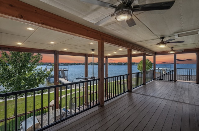 deck at dusk featuring a water view, a lawn, and ceiling fan